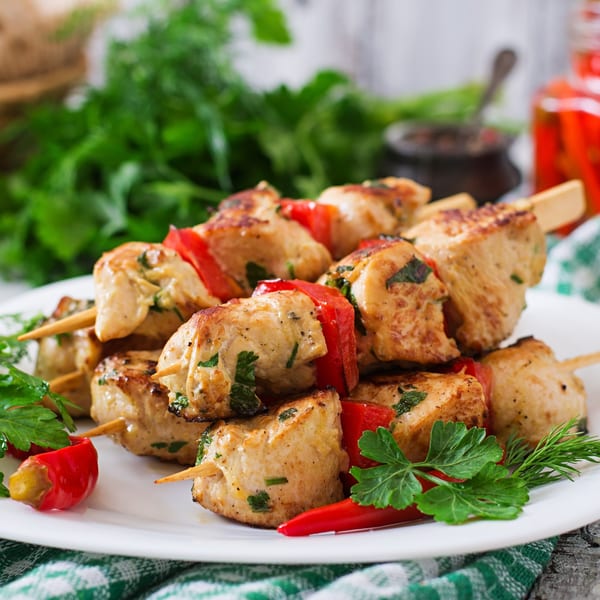 Chicken tikka skewers with red bell peppers and fresh herbs on a white plate.
