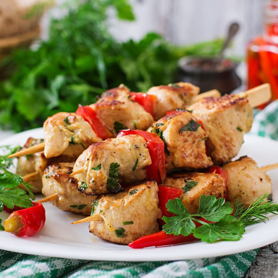 Chicken tikka skewers with red bell peppers and fresh herbs on a white plate.