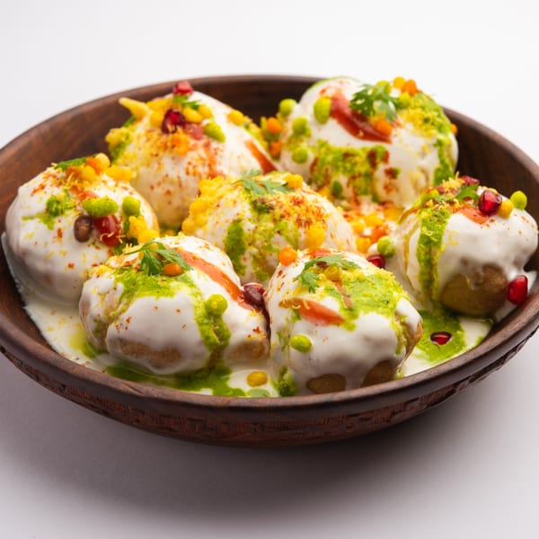 A wooden bowl filled with Little India Pizza® Dahi Vada, topped with yogurt, chutneys, and spices.