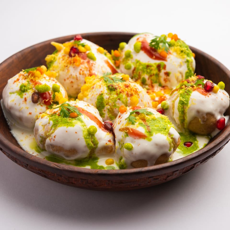 A wooden bowl filled with Little India Pizza® Dahi Vada, topped with yogurt, chutneys, and spices.