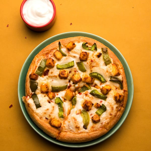 Little India Pizza's paneer and green bell pepper pizza on a green plate with a side of white sauce.