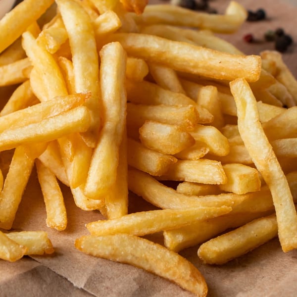 Close-up of golden, crispy french fries scattered on a brown paper surface.