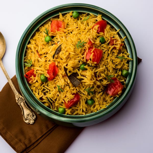 A green bowl of Indian tomato pulao rice with peas and cilantro, next to a golden spoon.