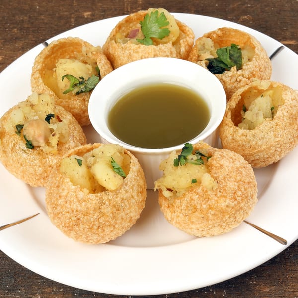 A plate of golden-fried pani puri shells filled with potato and chickpeas, served with green pani.