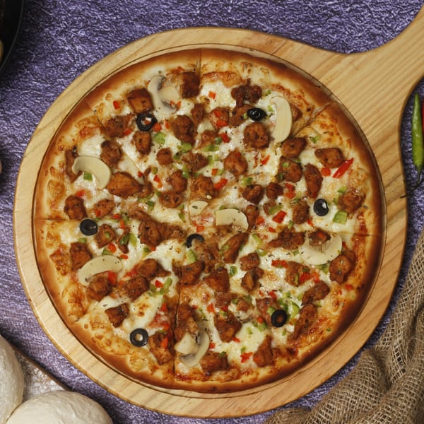 Little India Pizza's chicken tikka pizza with mushrooms, olives, and bell peppers on a wooden board.