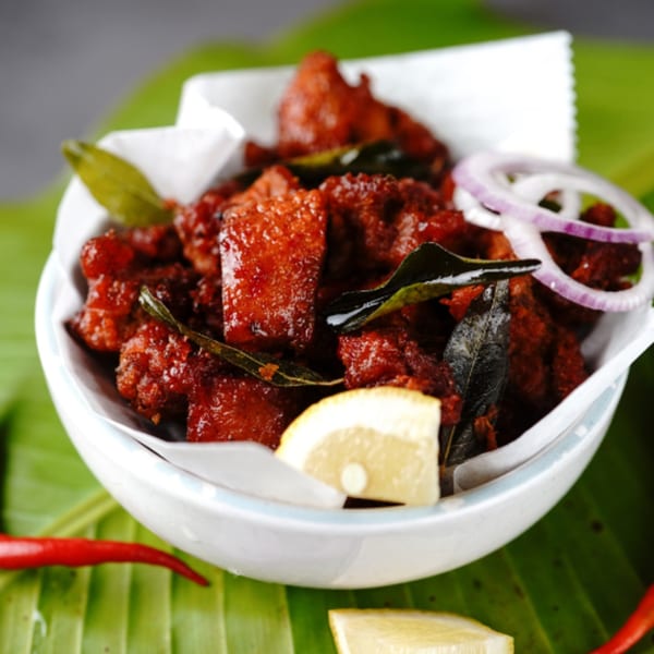 A white bowl of Little India Pizza®'s red Indian chicken, garnished with onions, lemon, and curry leaves.