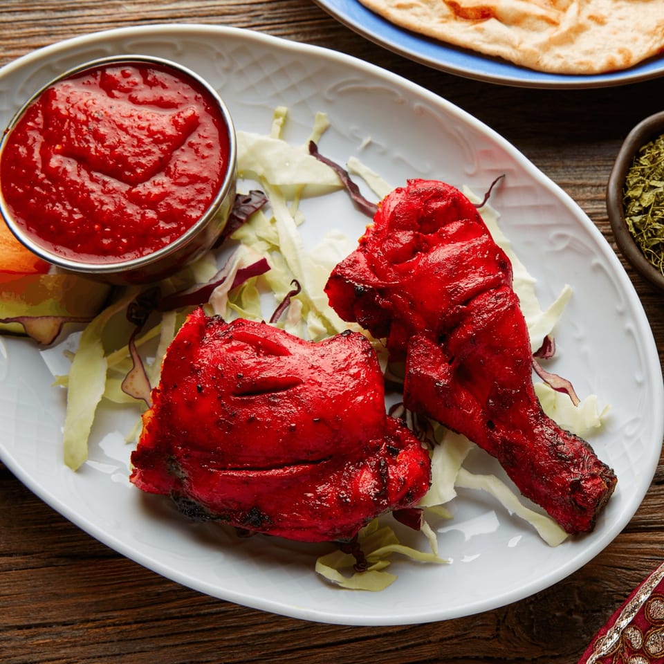 Two vibrant red tandoori chicken pieces with sauce and lettuce on a white plate.