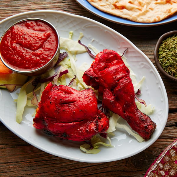 Two pieces of Little India Pizza® Tandoori Chicken with red sauce and shredded cabbage.